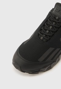 Μαύρο αθλητικό παπούτσι με κομψό σχέδιο, που συνδυάζει ομαλό συνθετικό υλικό και υφασμάτινη υφή. Διαθέτει ρίγες ίδιας απόχρωσης και ανθεκτική σόλα.