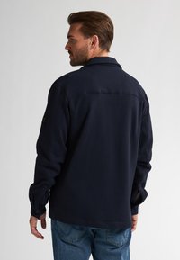Marineblauwe wollen jas met een kraag, knoopmanchetten en een rechte snit. Heeft een gestikte schoudernaad en een subtiele textuur.