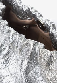Borsa metallica argento con una texture trapuntata, caratterizzata da un bordo superiore arricciato e una chiusura a bottone rotondo in metallo all'interno.