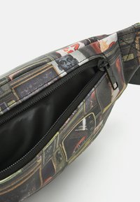 Vyötärölaatikko, jossa on kollaasi retro-televisiomalleista, pääasiassa mustana ja värikkäillä korostuksilla, kestävässä vetoketjukiinnityksessä ja teksturoidussa kankaassa.