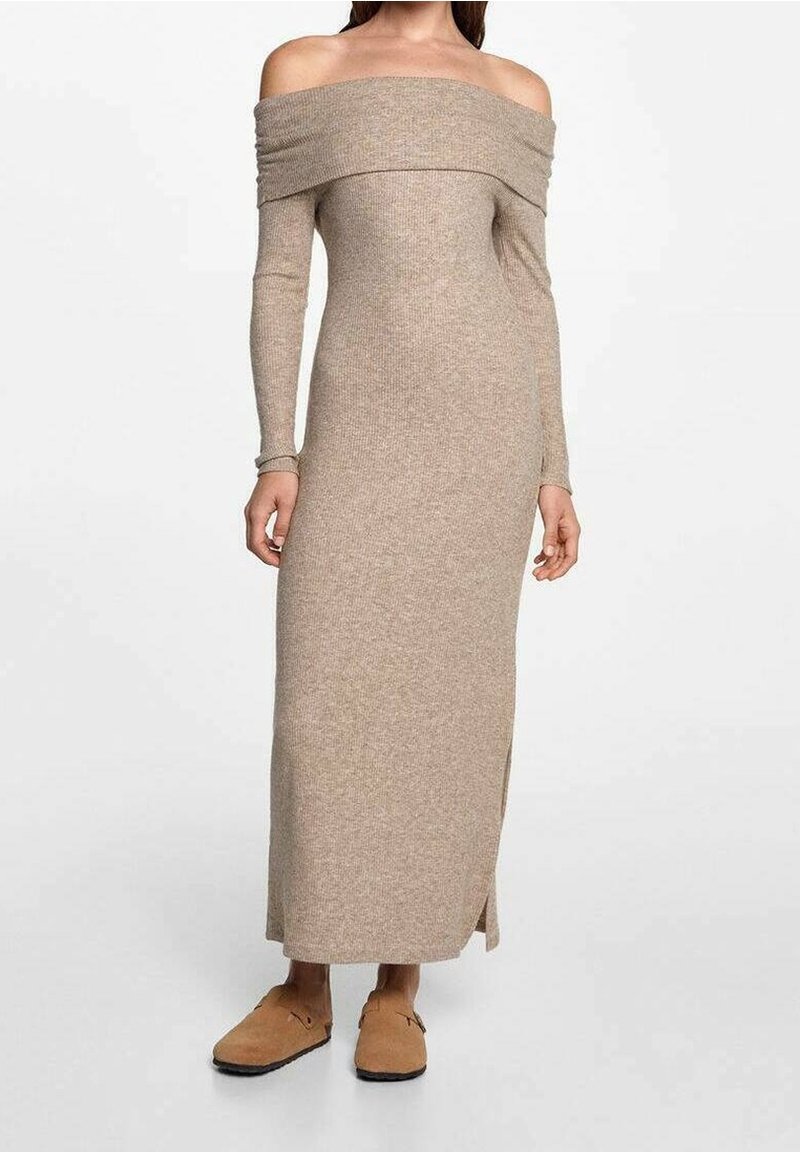 Femme portant une robe maxi en maille beige, épaules dénudées, manches longues, fente latérale et chaussures slip-on couleur camel.