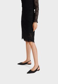 Ballerine slingback in pizzo nero con punta affusolata, caratterizzate da un design testurizzato e un delicato accento nude sulla cinghia del tallone. Suola piatta.