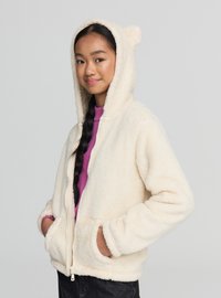 Kremowa, puszysta bluza z polaru z kapturem, zapinana na przedni zamek, z ozdobami przypominającymi uszy na kapturze oraz bocznymi kieszeniami. Nosi się ją na różowy top.