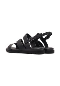 Black leather sandals featuring three wide straps, a buckled ankle strap, thick black sole, and a textured finish.