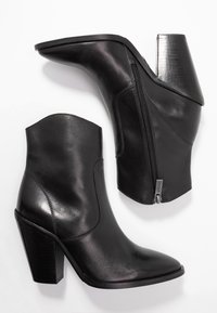 Botines de cuero negro hasta el tobillo con punta afilada, cierre de cremallera en el lateral y tacón grueso, que presentan una textura suave y un diseño elegante.