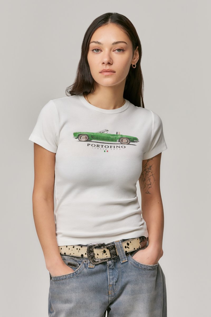 White short-sleeve t-shirt featuring a green vintage car graphic with "PORTOFINO ITALY 1972" text. Worn with blue denim jeans and a patterned belt.