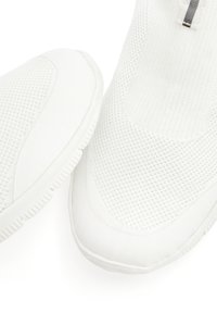 White athletic shoes with a textured knit upper, seamless design, flexible sole, and minimalistic accents.