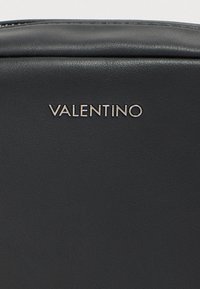Μαύρο δερμάτινο σακίδιο με απαλό υφή και μεταλλικό λογότυπο "VALENTINO" μπροστά. Απλός, μινιμαλιστικός σχεδιασμός.