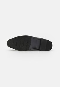 Suela de zapato de cuero negro con fondo de goma texturizada, que presenta patrones hexagonales para un mejor agarre y una forma de puntera redondeada. Diseño elegante con acentos sutiles.