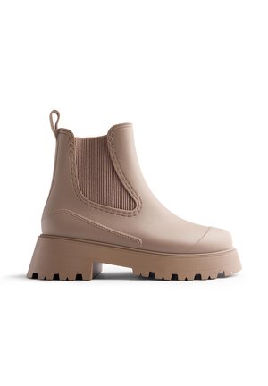 Bottines Chelsea beige à hauteur de cheville avec panneau latéral élastique, languette au talon et semelle épaisse avec relief.