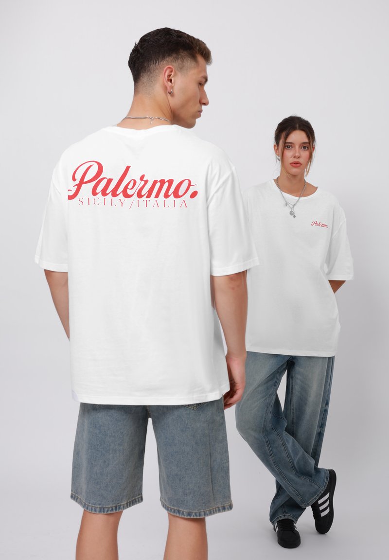 Biele oversized tričká majú na chrbte červenú grafiku "Palermo" a malú grafiku na prednej strane. Kombinujú sa so svetlo modrými denimovými šortkami a džínsami.
