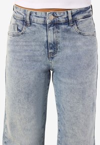 Svjetloplave traperice s visokom strukom, pet džepova, kontrastnim šavovima i dugmetom za zatvaranje na struku.