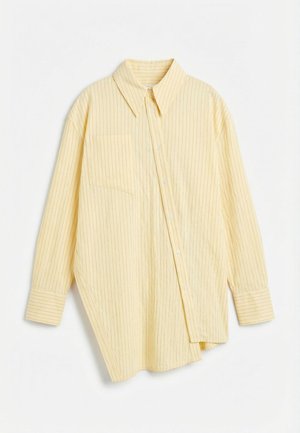 Lysegul langermet skjorte med tynne vertikale striper, asymmetrisk kant, brystlomme foran og knappestolpe foran på hvit bakgrunn.