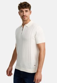 Polo de manga corta color crema, confeccionado en tejido de punto, con cuello con cremallera y rayas verticales texturizadas.