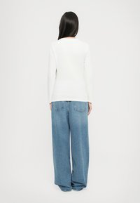 Hvit langermet topp kombinert med løse lyseblå denimjeans, med lommer og rett ben-design, sett fra baksiden.