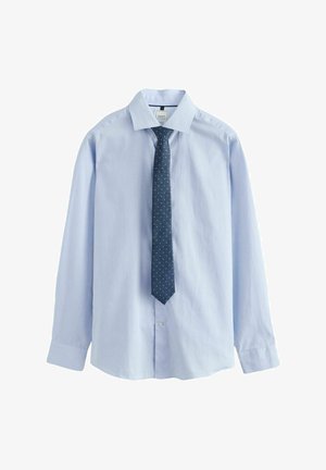 Camicia azzurra a maniche lunghe in cotone, con colletto classico e cravatta blu navy con pois bianchi, frontale e polsini con bottoni.