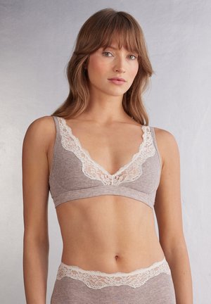 Lichtbruine bralette met kantafwerking, voorzien van een diepe V-hals en geribbelde textuur. Verstelbare bandjes zorgen voor extra comfort bij de zachte stof.