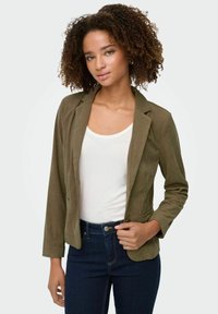 Olivgrüner Cord-Jackett mit tailliertem Design, reverskragen und langen Ärmeln, kombiniert mit einem weißen Oberteil und dunkelblauen Jeans.