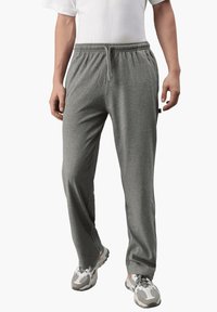 Graue Jogginghose mit elastischem Bund und Kordelzug, aus weichem Material, mit seitlichen Taschen und legerem Schnitt, kombiniert mit Turnschuhen.