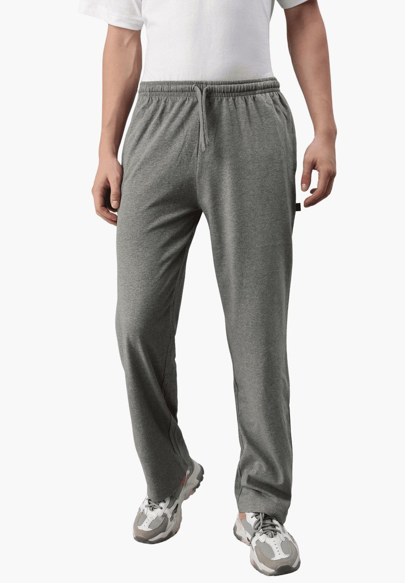 Graue Jogginghose mit elastischem Bund und Kordelzug, aus weichem Material, mit seitlichen Taschen und legerem Schnitt, kombiniert mit Turnschuhen.