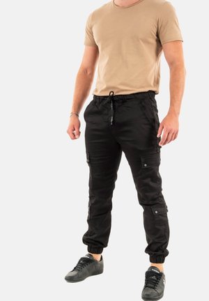 Pantaloni cargo neri con polsini elasticizzati e tasche, abbinati a una maglietta beige chiaro a maniche corte. Le sneakers sono nere. Design semplice e vestibilità comoda.
