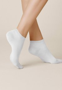 Weiße Knöchelsocken, die an einem Fuß präsentiert werden, aus einem glatten Stoff mit einem gerippten Bündchen, das einen subtilen Glanz und eine leichte Textur zeigt.