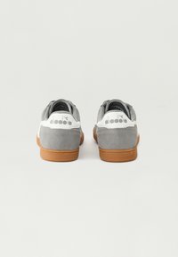 Grå semsket sneakers med en hvit hælkrage og gummisåle. Har et lite ikon på hælen og et polstret mansjett for komfort.