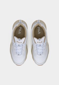 Λευκά και μπεζ αθλητικά παπούτσια FILA με κορδόνια, φωτογραφημένα από ψηλά πάνω σε απλό φόντο.