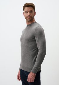 Pull-over gris à manches longues avec un col rond et des poignets côtelés, fabriqué à partir d'un tissu tricoté doux et texturé. Porté sur un pantalon sombre.