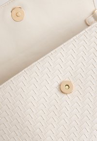 Cream-colored woven leather bag with gold-tone magnetic snap closure and smooth interior lining.