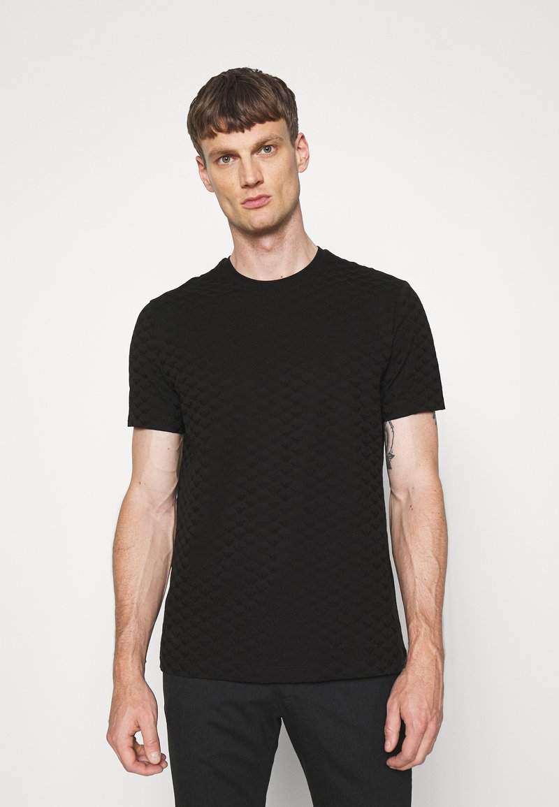 Camiseta de manga corta negra con un patrón texturizado que recuerda a pequeños corazones. Cuello redondo, corte ajustado, fabricada en una tela suave y lisa.