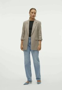 Blazer gris clair, haut noir et jeans bleu clair. Le blazer a une coupe décontractée avec des manches retroussées ; des escarpins bleus à bout pointu complètent le look.