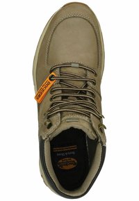 Brauner Lederschuh mit gepolstertem Kragen, verstärkten Ösen und braunen Schnürsenkeln. Mit einem orangefarbenen Etikett und einer robusten Gummisohle ausgestattet.