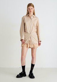 Gestreepte beige button-up shirt met lange mouwen, gecombineerd met een romige rokken met ruches, zwarte kniekousen en chunky zwarte schoenen.