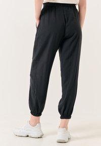 Zwarte, lichtgewicht joggers met elastische boorden en tailleband, voorzien van zijzakken en een soepele textuur. Gemaakt met witte sneakers.