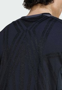 Tamno atletska majica s teksturiranim, sjajnim crnim geometrijskim uzorkom na leđima. Lagana tkanina s glatkom završnom obradom, okrugli izrez.