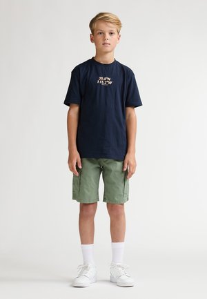 Donkerblauw katoenen T-shirt met gedrukte coördinaten, gecombineerd met groene cargoshorts. Witte sokken en sneakers maken de outfit compleet. Eenvoudig, casual ontwerp.