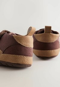 Chaussures en daim brun avec des accents beige, présentant une forme arrondie, des détails de couture et une languette à l'arrière pour un enfilage facile.