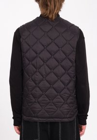 Chaleco negro acolchado con patrón de diamantes, con cuello alto y diseño sin mangas. Textura suave con aislamiento ligero.