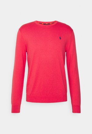 Pull à col rond rouge à manches longues avec petit logo brodé bleu marine sur la poitrine gauche, présenté sur un fond gris clair uni.