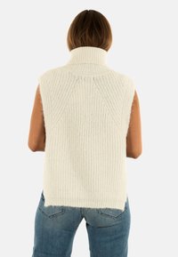 Maglione senza maniche bianco in maglia, con colletto alto, caratterizzato da una texture a coste e un orlo posteriore leggermente più lungo.