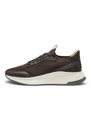 Basket en maille et cuir marron foncé avec une semelle blanche texturée et une languette beige au talon, vue de côté sur fond blanc.