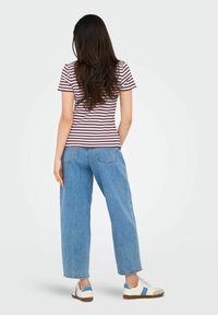 Bordeauxrode en witte gestreepte T-shirt, gecombineerd met hoog getailleerde, losse blauwe jeans en witte sneakers met blauwe en bruine accenten.