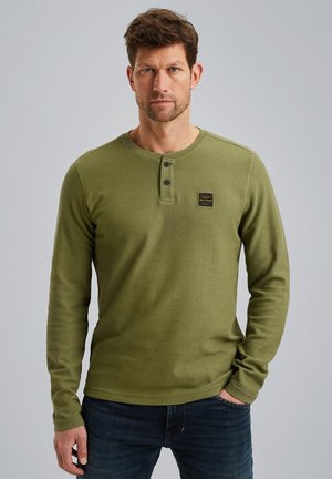 Maglietta henley verde a maniche lunghe in tessuto rigato con collo rotondo, abbottonatura a tre bottoni e una piccola etichetta con logo sul petto.