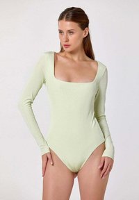 Bodysuit à manches longues en doux tissu vert clair, avec un col carré et une coupe ajustée, au toucher lisse et à la finition minimaliste.