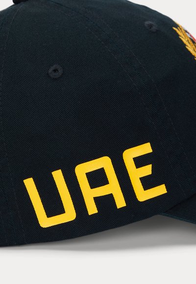 Cappello nero con la scritta gialla "UAE" sul frontale. Realizzato in tessuto, ha una forma strutturata e un foro di ventilazione cucito sulla parte superiore.