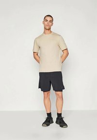 Beež lühikeste varrukatega särk, mis on paaritatud mustade lühikesed püksid ja spordijalatsitega. Kanga pind näeb välja sile ning särgil on peene logo detail.