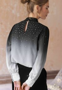 Schwarz-weiße Gradient-Bluse mit Perlenverzierungen. Ausgestattet mit einem hohen Kragen, einem Schlüsselloch-Rücken und geknöpften Manschetten. Weicher, strukturierten Stoff.