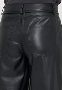 Pantalons en cuir noir avec une texture lisse, présentant une taille haute et deux poches arrière, conçus avec des détails de couture sur mesure.