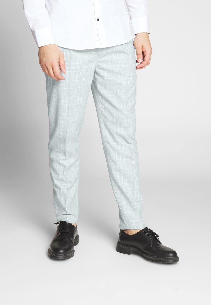 Světlé šedé kostkované kalhoty v slim fit. Vyrobené z hladké látky. Nosené s černými šněrovacími botami.